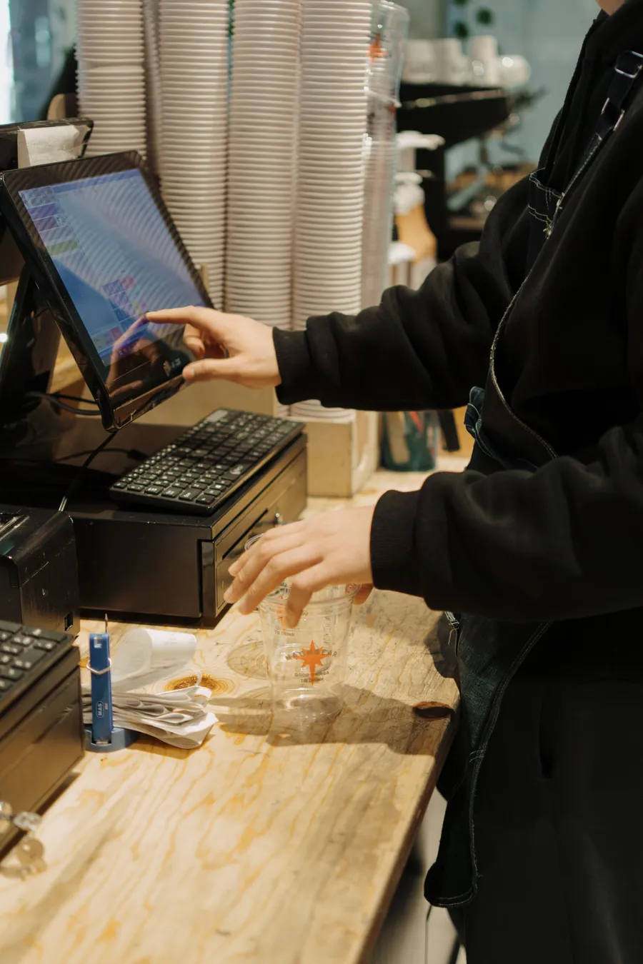 A retail employee using a till at a busy coffee counter